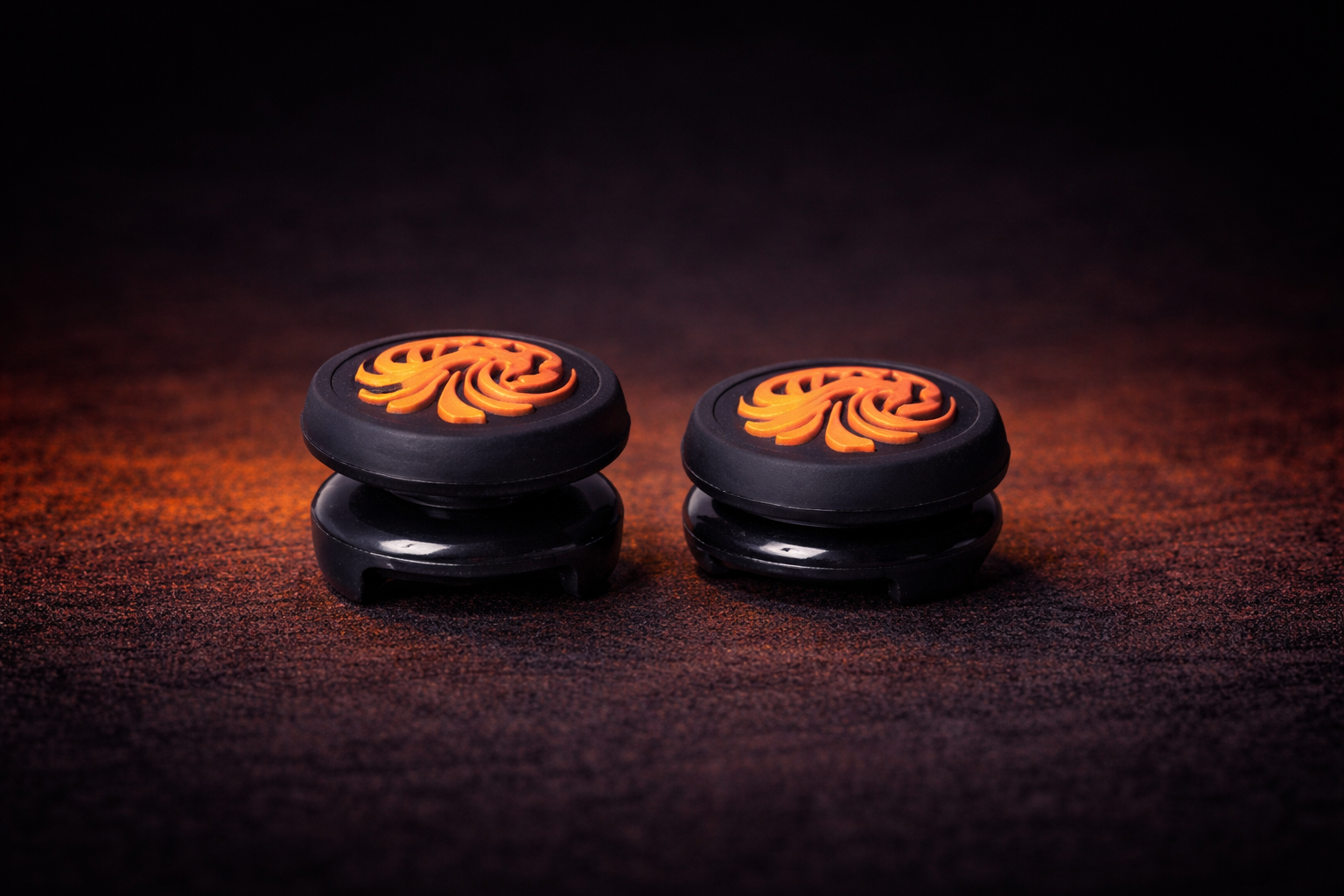 Two black and orange gaming controller buttons on a dark surface